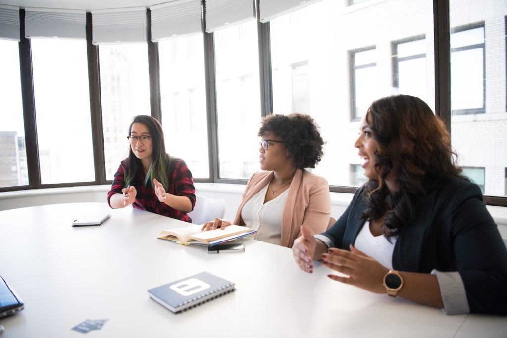 three women sit at a table in a mediation meeting